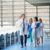 a group of doctors and nurses talk while walking down a hospital hall